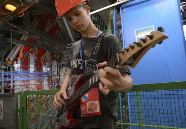 Джона Кон играет на гитаре в ЦЕРНе на фоне коллайдера