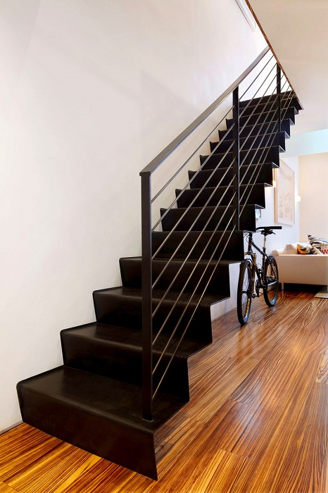 Массивная металлическая лестница с чёрными ступеньками и перилами, которая контрастным пятном выделяется на фоне светлого интерьера.
