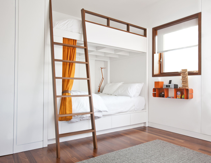 Небольшая уютная спальная комната с белыми стенами и двухэтажной кроватью с выдвижными ящиками.