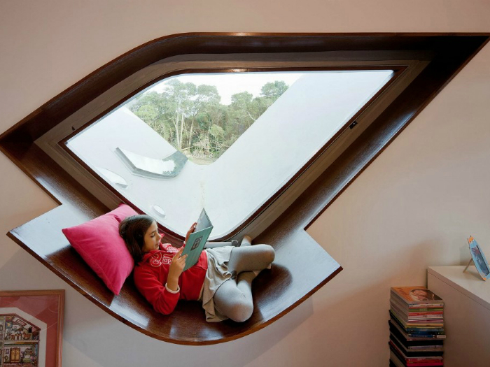 Окно оригинальной формы и подоконник, оборудованный для чтения и отдыха.