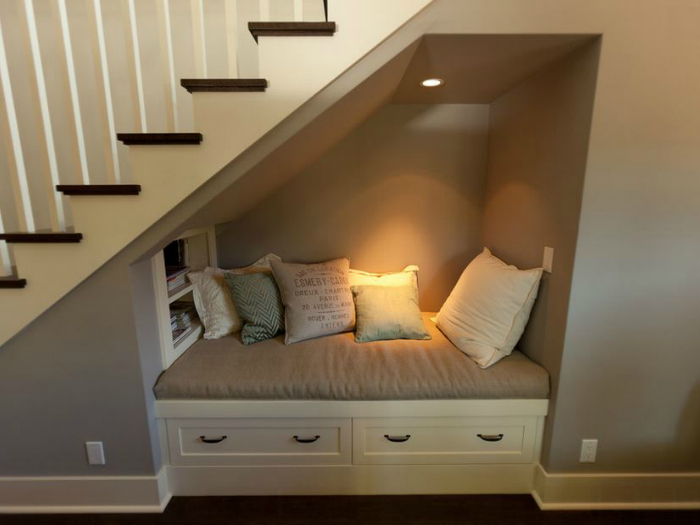 Пространство под лестницей можно оборудовать небольшим диванчиком и светильником.