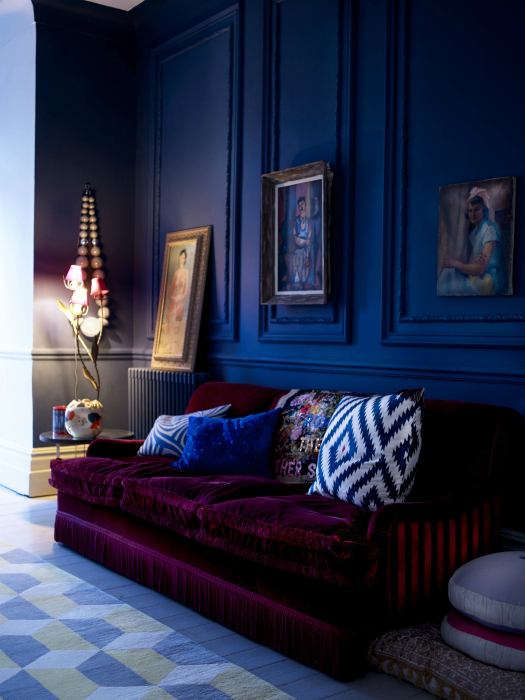 Гостиная с синими стенами и бордовым диваном.