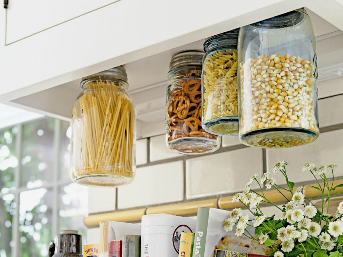 Печенье, специи и крупы удобно хранить в обыкновенных стеклянных банках, прикрученных к нижним частям полок и шкафчиков.