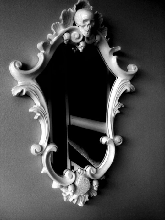 Зеркало необычной формы в белой раме, украшенной черепом.