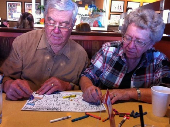 Пожилая пара разукрашивает картинки в детской книжке, ожидая свой заказ в ресторане.
