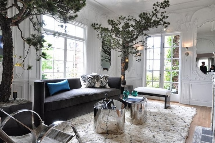 Причудливый интерьер гостиной комнаты с невероятными деревьями по углам и симпатичными круглыми столиками.