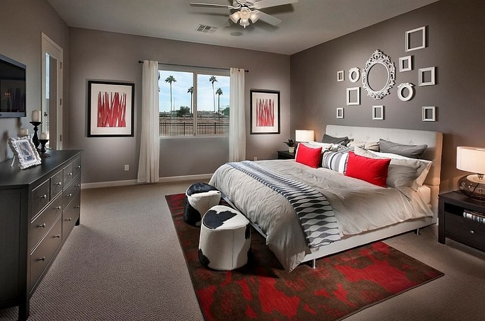 Спальня в серых тонах инкрустирована с помощью красных элементов в интерьере и белых рамок на стене, которые отлично вписываются в интерьер.