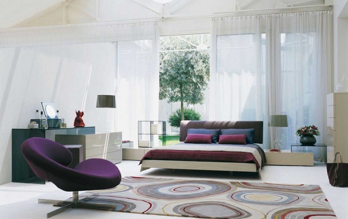Спальня украшена ковром с симпатичными кругами и с яркими подушками на диване.