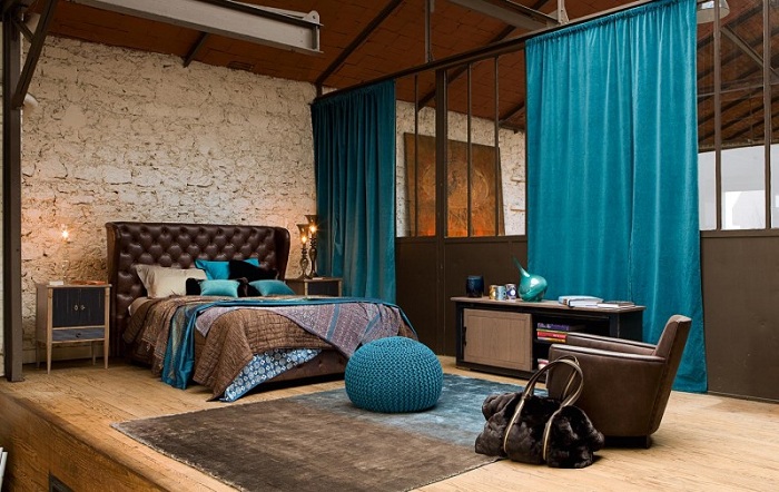 Симпатичная спальня с каменной стеной и с синими элементами в интерьере.