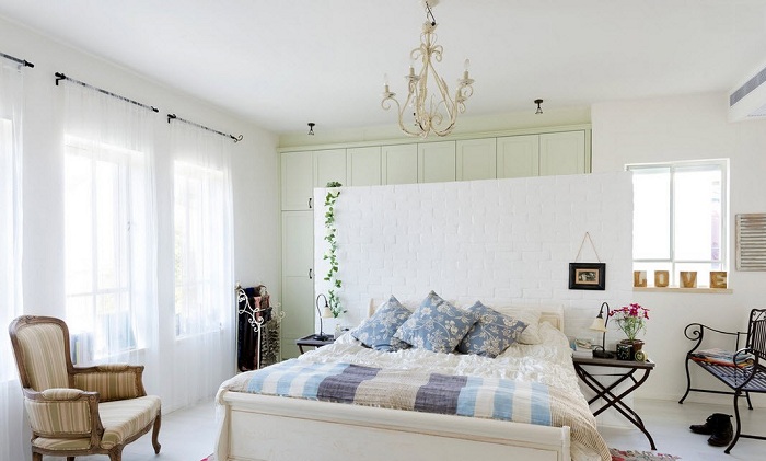 Традиционный светлый интерьер спальни разбавлен яркими акцентами цветочного текстиля и витой мебелью.