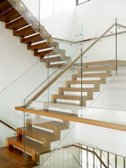 Стильная деревянная лестница с стеклянными перилами и несколькими пролетами.