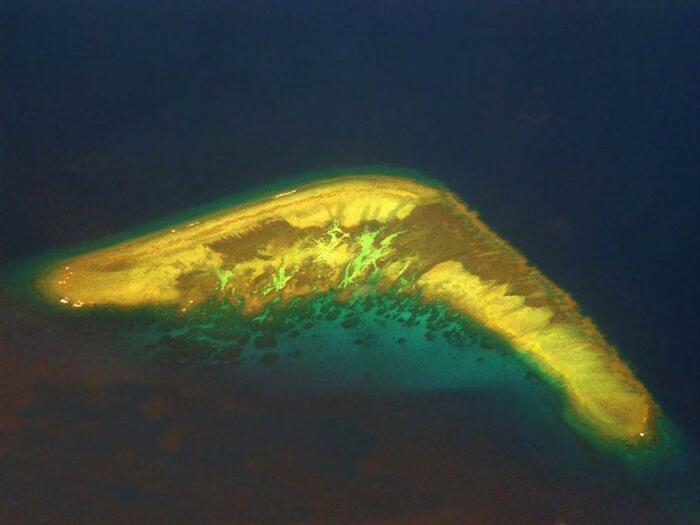 Остров-бумеранг имеет не только причудливую форму, но и постоянно меняет цвет (архипелаг Спратли). | Фото: russian.china.org.cn.