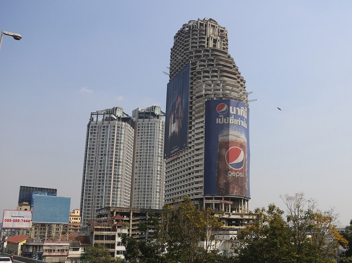 Только рекламные плакаты скрашивают серость и угрюмость полуразрушенных стен, а владельцам приносят какой-никакой доход (Sathorn Unique Tower, Бангкок). | Фото: theislandlogic.com.